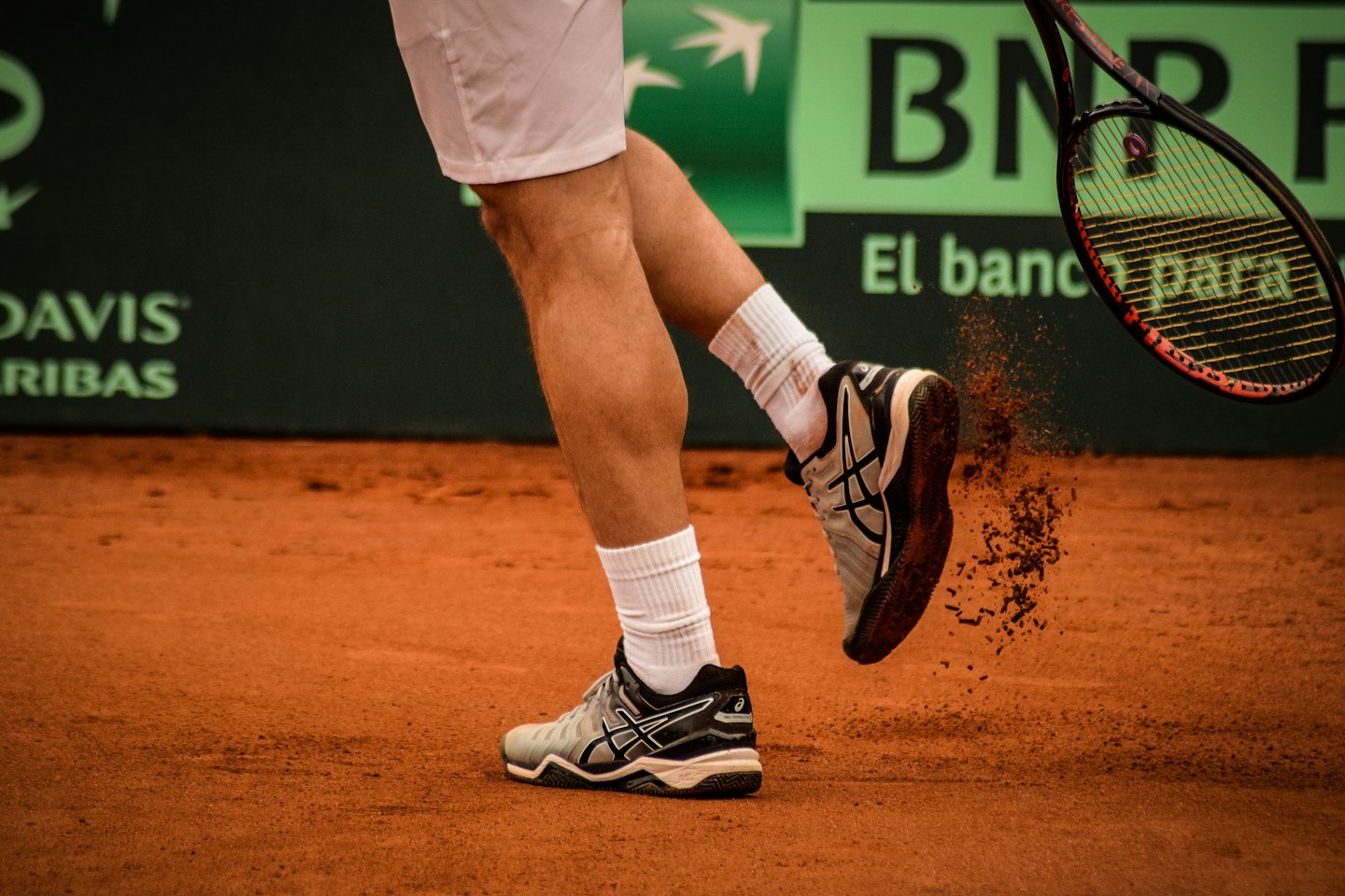 Piernas de tenista levantando arcilla en la cancha.