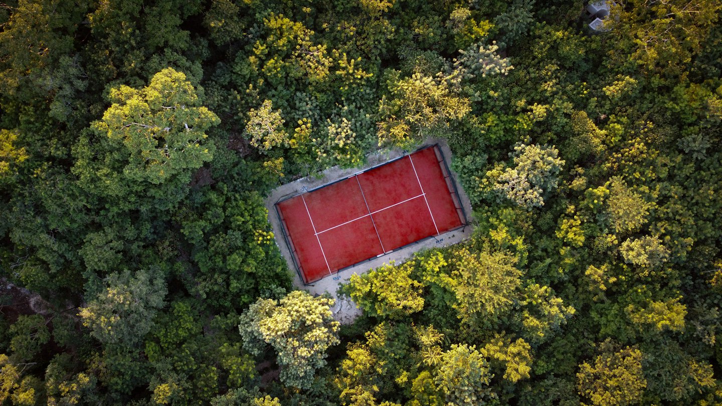 Una cancha de tenis roja se encuentra apartada en un bosque denso.